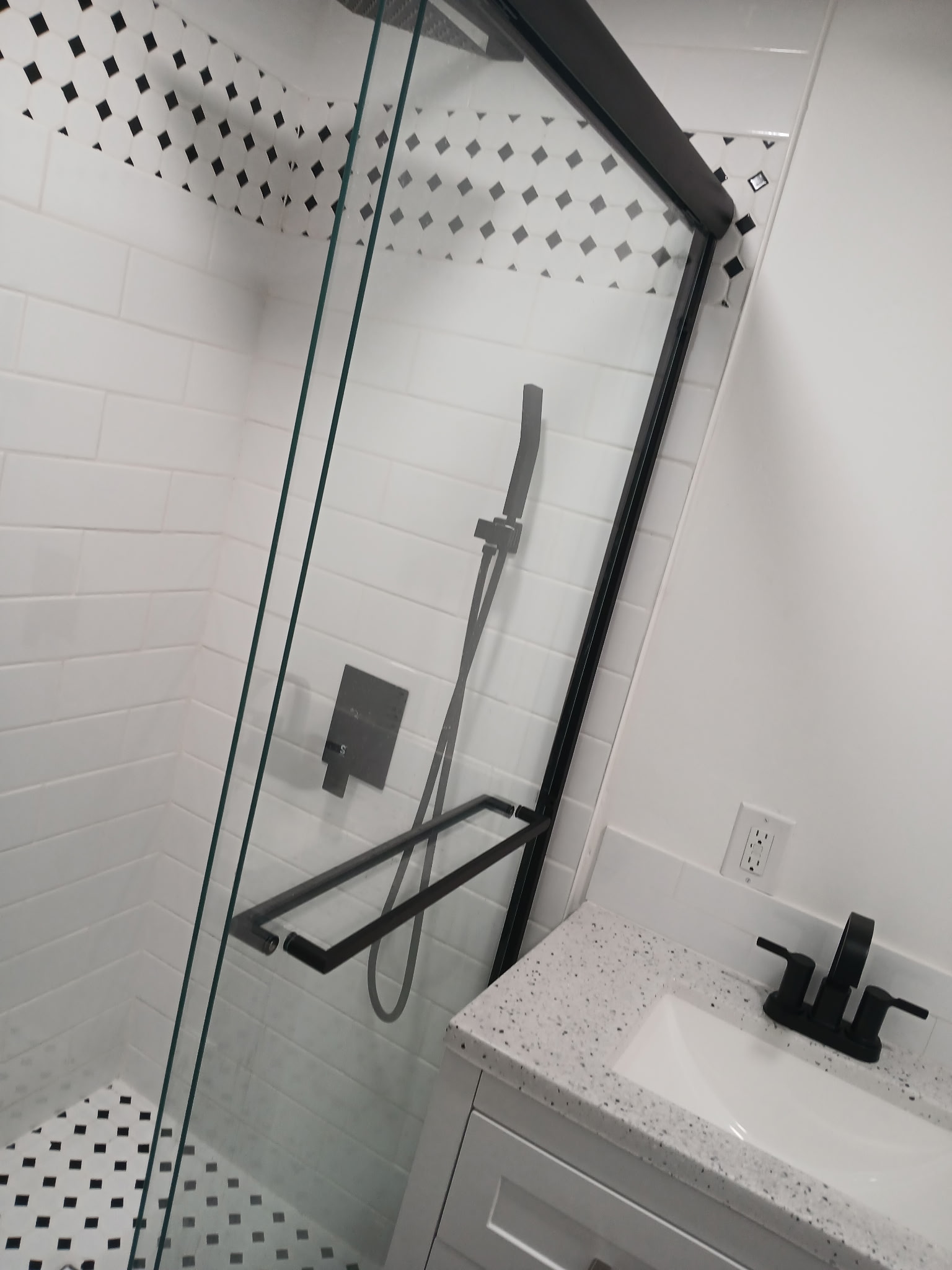 Black and white tile shower with diamond mosaic accent border and frameless glass enclosure