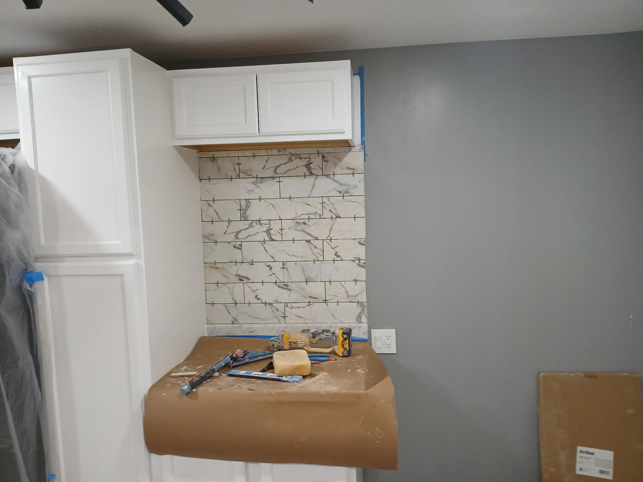 Marble-look tile backsplash being installed in kitchen with white cabinetry