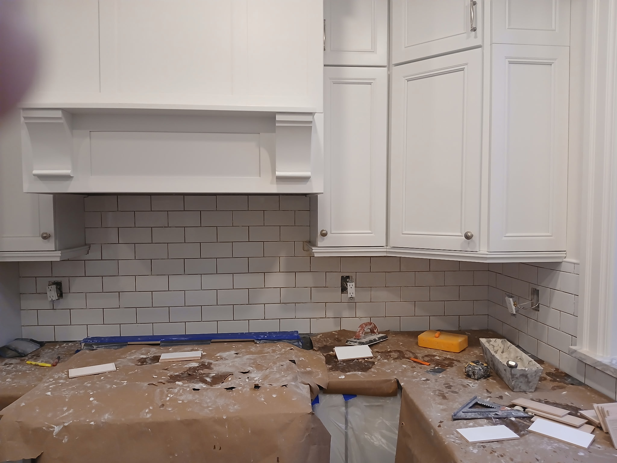 White subway tile backsplash installed under kitchen range hood with white cabinetry